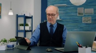 Aynı anda tablet ve dizüstü bilgisayar kullanan yaşlı bir adam mali grafikleri karşılıyor