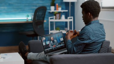 İnternet konferansında iş arkadaşlarıyla sohbet etmek için bilgisayarı açan siyahi bir adam.