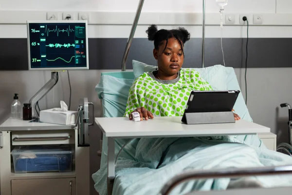 Afrykański amerykański młody pacjent odpoczywający w łóżku po operacji medycznej oglądający zabawny film — Zdjęcie stockowe