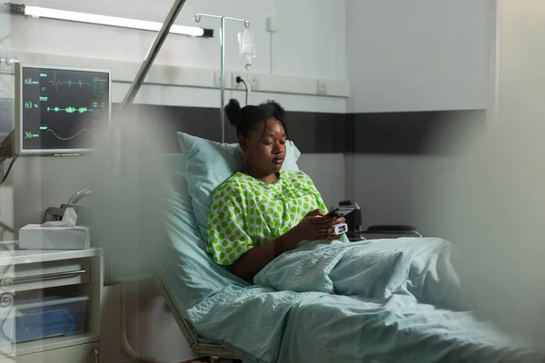 Patient malade afro-américain couché au lit tenant téléphone moderne navigation sur Internet — Photo