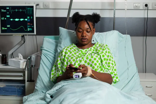 Afro-américain jeune patient se reposant dans le lit tenant smartphone moderne — Photo