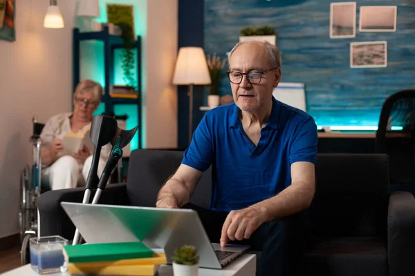 Uomo anziano utilizzando il computer portatile sul tavolo in soggiorno — Foto Stock