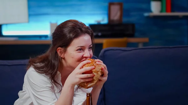 Ung människa skrattar åt TV medan hon äter hamburgare — Stockfoto