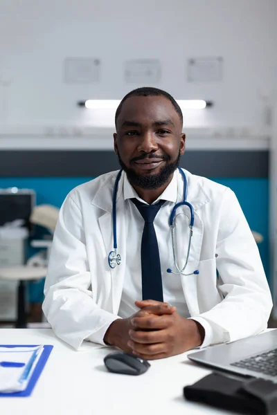 Retrato de médico praticante afro-americano sentado à mesa no escritório do hospital — Fotografia de Stock