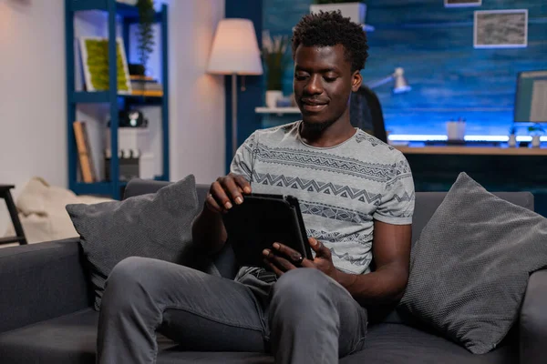 Afroamericano freelancer sentado en sofá celebración tableta ordenador —  Fotos de Stock