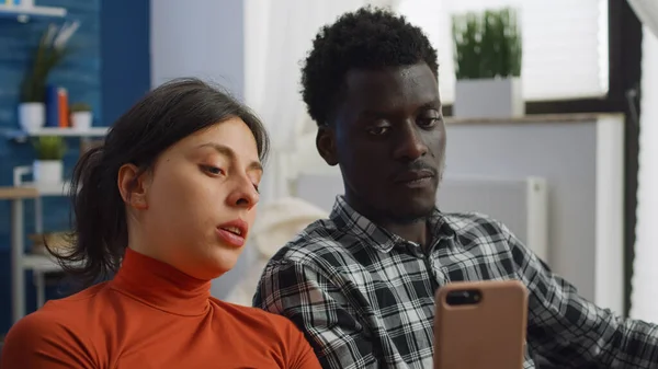Primer plano de la pareja de raza mixta utilizando el teléfono inteligente en casa —  Fotos de Stock