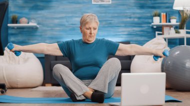 Emekli kadın, kol kaslarını çalıştırmak için dambıl kullanıyor.