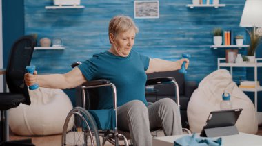 Yaşlı yetişkin tekerlekli sandalyede oturuyor ve ağırlık çalışıyor.