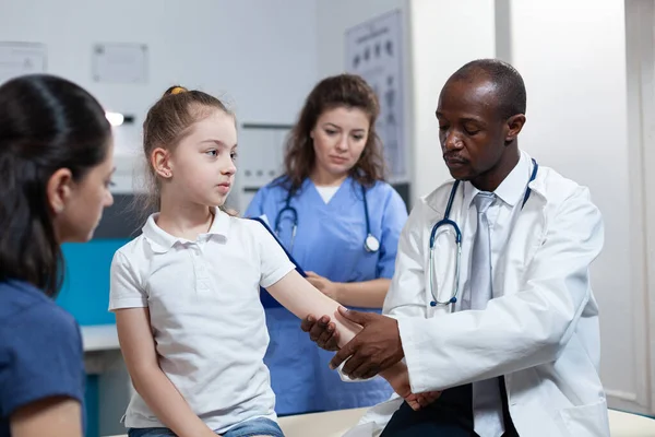 Médico pediatra afroamericano vendaje fracturado hueso de paciente niña — Foto de Stock