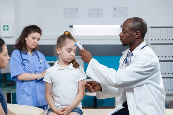 Médico pediatra afro-americano colocando termômetro infravermelho médico — Fotografia de Stock