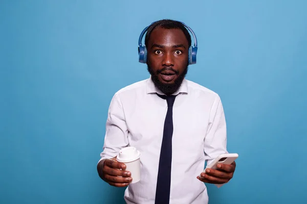 Hombre sorprendido escuchando música en auriculares inalámbricos mientras sostiene el teléfono inteligente — Foto de Stock