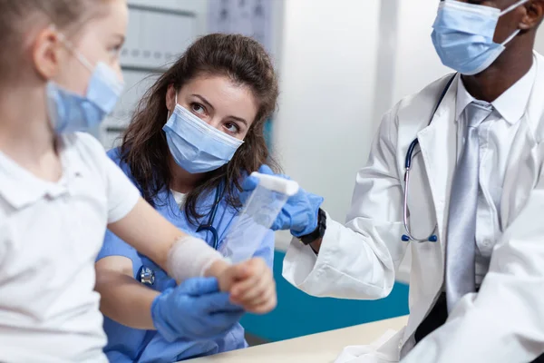 Médico asisstant ajudando médico pediatra afro-americano a enfaixar braço quebrado — Fotografia de Stock