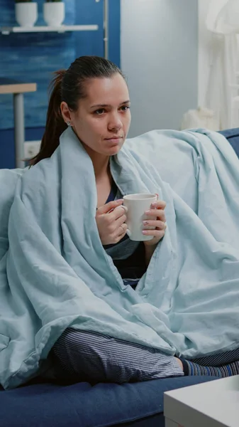 Chory kobieta trzyma filiżankę herbaty i siedzi w kocu — Zdjęcie stockowe