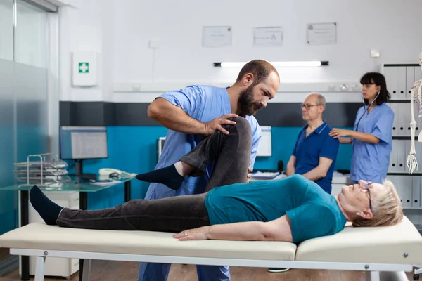 Kayropraktik uzmanı yaşlı kadına bacak yaralanmasında yardım ediyor.