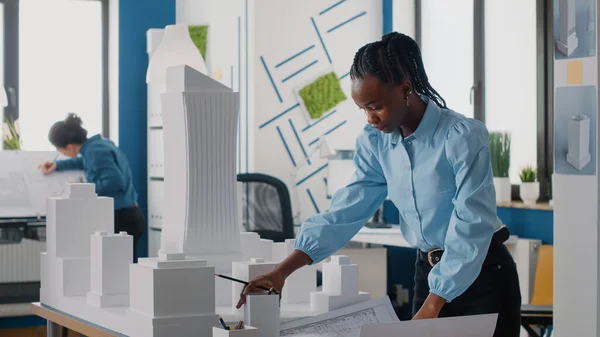 Mujer afroamericana analizando planos plan y modelo de construcción para trabajar en arquitectura — Foto de Stock