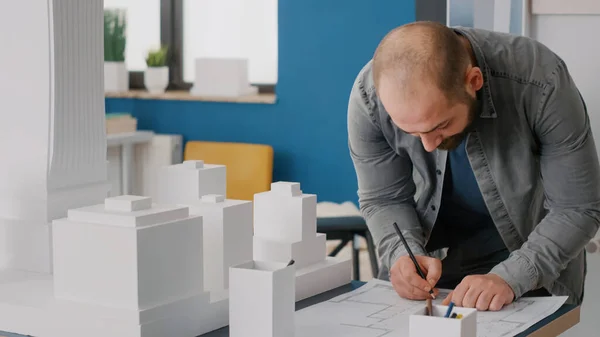 Close up of architect taking notes on blueprints plan to work on building model and maquette — Fotografia de Stock