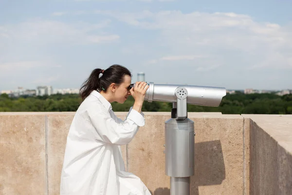 Vit kvinna står på taket och tittar genom teleskopet. — Stockfoto