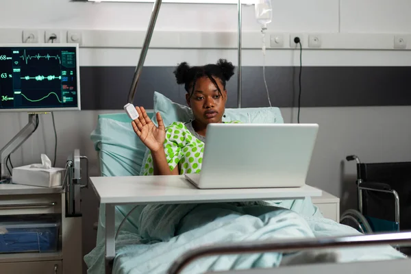 Afro-americano jovem paciente descansando na cama cumprimentando amigo remoto — Fotografia de Stock