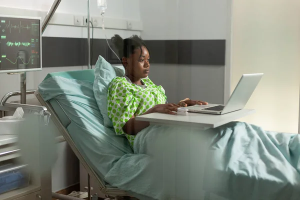 Αφροαμερικανός ασθενής που αναπαύεται στο κρεβάτι βλέποντας online κωμική ταινία στο laptop — Φωτογραφία Αρχείου