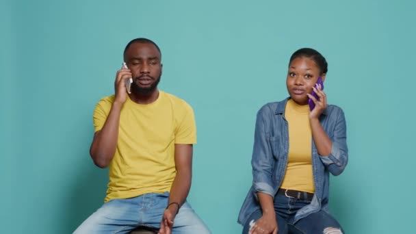 Man and woman talking on phone call together and sitting over blue background — Stockvideo