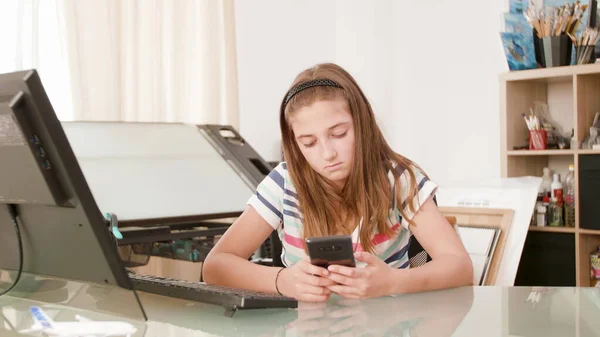 Portret młodej nastolatki siedzącej przy biurku na smartfonie — Zdjęcie stockowe