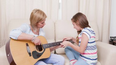 Ana gutarist kızıyla kanepede oturup gitar çalmayı öğretiyor.