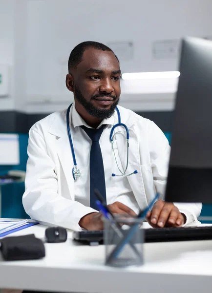 Médico especialista afro-americano analisando a experiência de doença on-line no computador — Fotografia de Stock