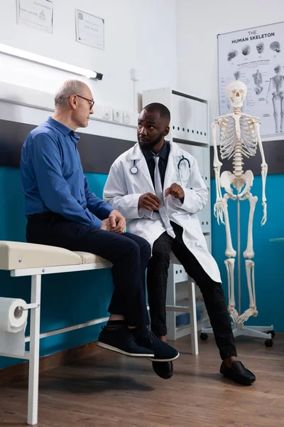 Retired old man discussing sickness symptoms to specialist therapist during medical appointment — Stockfoto