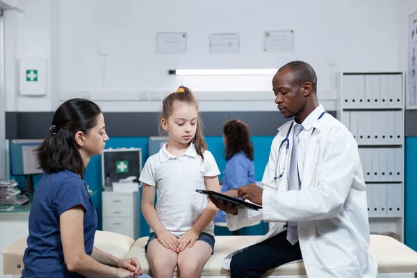 Médico pediatra afroamericano escribiendo síntomas de enfermedad de un niño pequeño — Foto de Stock