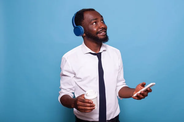 Homem sorridente de camisa branca olhando para cima segurando smartphone streaming de música para fones de ouvido sem fio — Fotografia de Stock