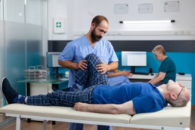 Fizyoterapist, bacağından yaralanan yaşlı adama iyileşmesi için yardım ediyor.