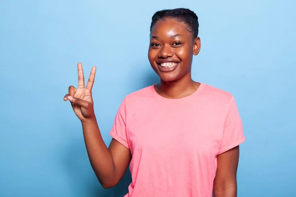 Gülümseyen Afrikalı Amerikalı genç bir kadının portresi parmaklarıyla barış sembolü yapıyor. — Stok fotoğraf