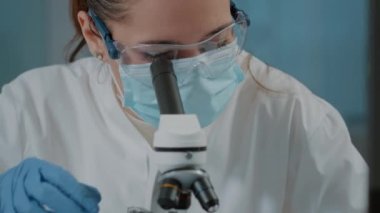 Yüz maskesi olan bir biyolog deney için mikroskop kullanıyor.