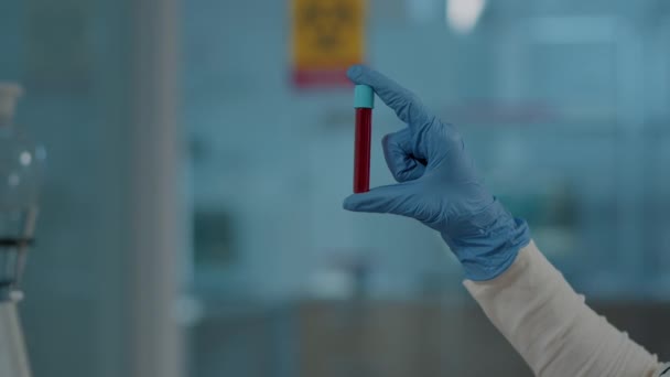 Laboratóriumi dolgozó, aki a vörös anyagot kémcsőben tartja tudományos elemzés céljából — Stock videók