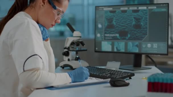 Microbiologo prendere appunti su carta e analizzare il DNA sul computer — Video Stock