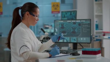 Biyolog test tüpündeki sıvıyı analiz ediyor ve bilgisayar kullanıyor.