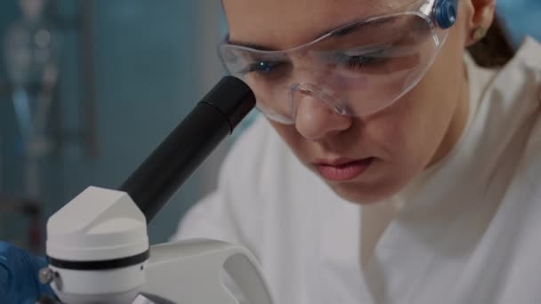 Vrouw die door microscoop lens kijkt om DNA monster te analyseren — Stockvideo