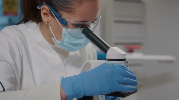 Βιολόγος με μάσκα προσώπου χρησιμοποιώντας μικροσκόπιο σε επιστημονικό εργαστήριο — Αρχείο Βίντεο
