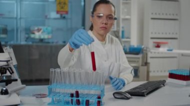 Mikrobiyolog laboratuarda kırmızı maddeyle test tüpünü analiz ediyor.