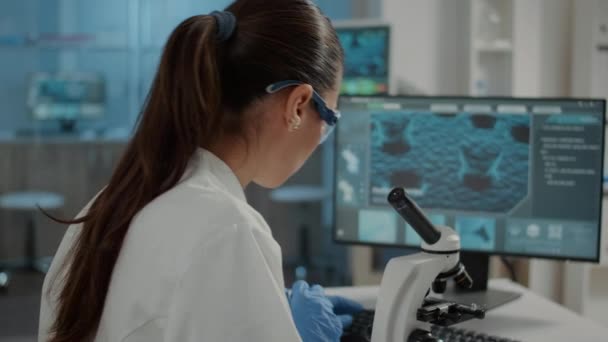 Женщина, изучающая образец ДНК на подносе микроскопа в лаборатории — стоковое видео