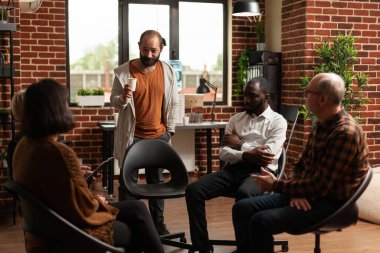 Adsız Alkolikler terapi seansındaki insanlarla ilerleme ve başarı hakkında konuşan bir adam.