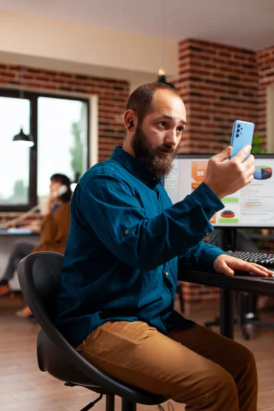 Uomo d'affari seduto alla scrivania con smartphone che legge messaggi e-mail con amici remoti — Foto Stock