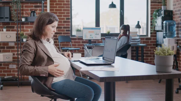 Mulher de negócios grávida trabalhando no laptop usando documentos para estratégia de marketing — Fotografia de Stock