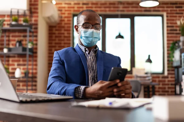 Ofiste koronavirüs salgını sırasında projeyi planlamak için dokunmatik ekranlı cep telefonuyla çalışan kişi