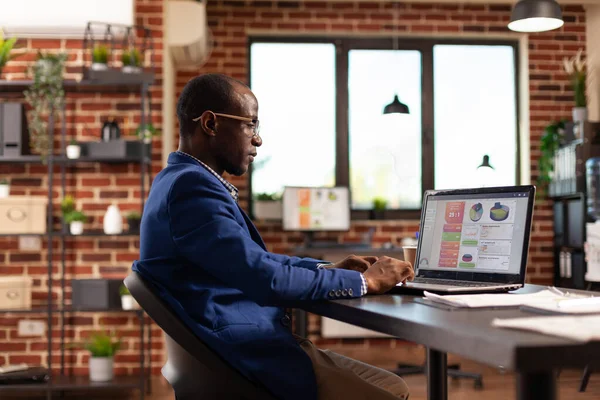 Impiegato afroamericano che utilizza il laptop per analizzare i grafici aziendali e la crescita aziendale — Foto Stock