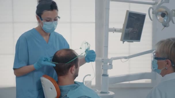 Ассистент стоматолога использует кислородную маску для обезболивания пациента — стоковое видео