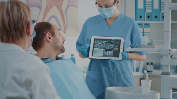Krankenschwester und Patient analysieren Prothesenröntgenbild im Zahnarztkabinett — Stockvideo