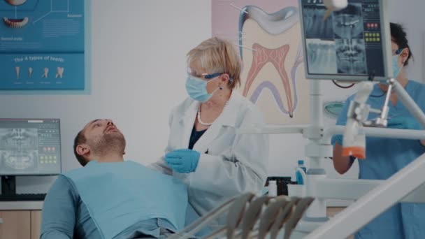 Tandarts met gezichtsmasker met behulp van tandheelkundige hulpmiddelen om kunstgebit te onderzoeken — Stockvideo