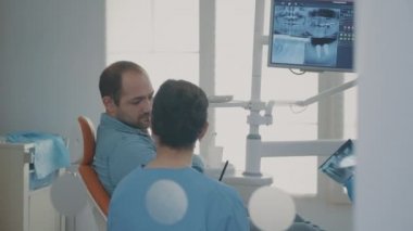 Diş hekimi ve hemşire diş ağrısı olan hastaya röntgen taramasını açıklar.