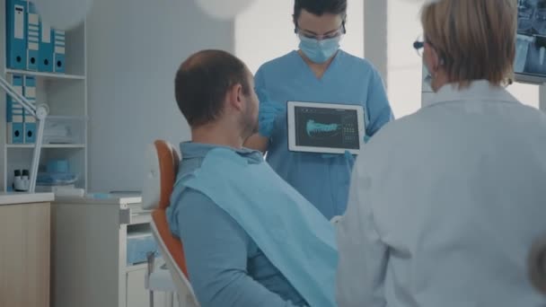 Fogszabályozó nővér, aki röntgen eredményeket tart a tablettán, hogy mutassa a beteget — Stock videók